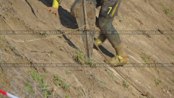 The navigator of an off-road crew is climbing a steep slope. A man is pulling a winch anchor behind him. A close-up of the athlete's legs and anchor. Off-road racing. Стоковое видео, видеограф Воловодов Владимир / Фотобанк Лори