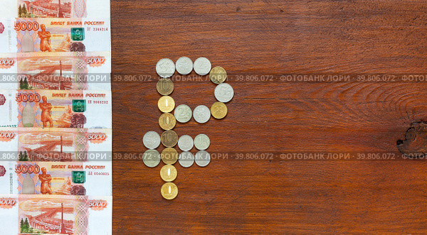 The symbol of Russian currency Ruble is made of ruble coins and a row of paper banknotes of 5000 rubles on wooden background. Money  and finance concept. Top view, copy space, flat lay, mock up. Стоковое фото, фотограф Виктория Катьянова / Фотобанк Лори