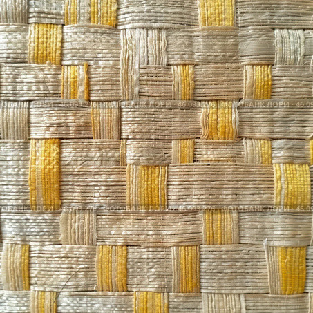 The texture of a woven material made from natural fibers such as straw, reed or palm leaves. The weave has a checkerboard pattern, with alternating stripes of beige and yellow. The surface has a slightly glossy appearance, with visible fibers and natural irregularities, giving it an authentic and rustic look. This texture is typical of traditional handicrafts such as mats, baskets, rugs and straw hats. Стоковое AI-изображение, AI-художник Анна Кривицкая / Фотобанк Лори