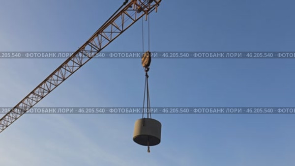 The tower crane slowly and confidently lifts the massive concrete ring. The ring is moved to the storage warehouse, the cargo hangs on strong cables while the crane carefully moves. Стоковое видео, видеограф Скрипачев Антон / Фотобанк Лори