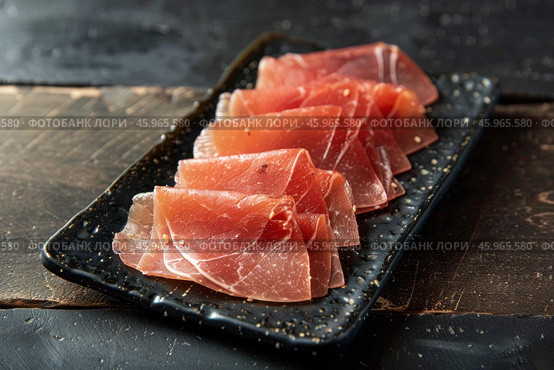 Thin slices of coppa on a black rectangular plate resting on a dark wooden table. Стоковое AI-изображение, AI-художник Иван Рябоконь / Фотобанк Лори