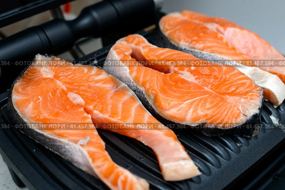 Three raw salmon steaks are toasted on a modern electric non-stick coating grill. Healthy eating concept. Close up photo with selective focus. Три стейка из сырого лосося поджариваются на современном электрическом гриле с антипригарным покрытием. Концепция здорового питания. Фотография крупным планом с выборочным фокусом. Стоковое фото, фотограф Дмитрий Березнев / Фотобанк Лори
