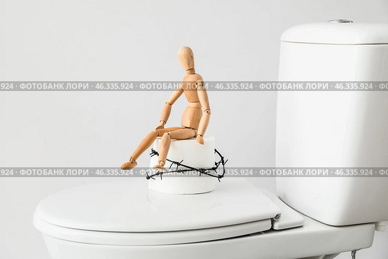 Toilet bowl with roll of paper, barbed wire and wooden human figure on light background. Hemorrhoids concept. Стоковое фото, фотограф Pixel_shot / Фотобанк Лори