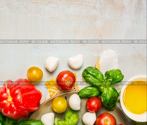Tomatoes, mozzarella balls with basil leaves and oil in white bowl on rustic wooden background, top view, place for text. Стоковое фото, агентство Ingram Publishing / Фотобанк Лори