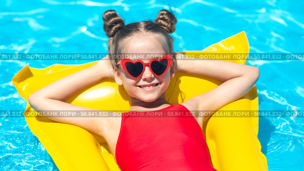 Top view little girl in red swimsuit lies comfortably on yellow inflatable mattress in swimming pool with blue water on summer day on tropical vacation. Relaxation, fun, carefree childhood concept. Стоковое фото, фотограф Ирина Михайличенко / Фотобанк Лори