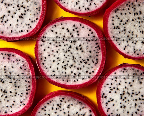 Top view of tropical exotic cut round slices of Dragon fruit or Pitaya on a yellow background. Close-up view.. Close up view of background from round slices of Dragon fruit or Pitaya on a yellow background. Стоковое фото, агентство Ingram Publishing / Фотобанк Лори