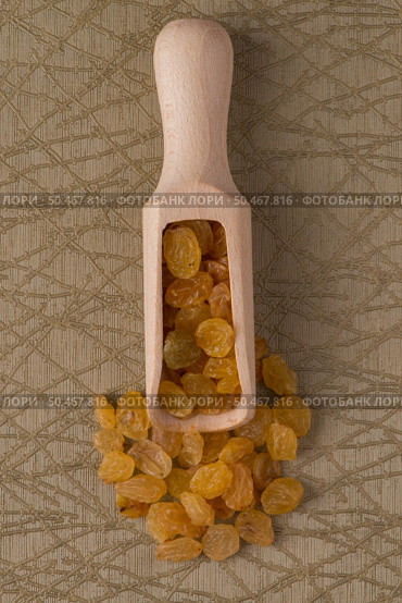 Top view of wooden scoop with golden raisins against green vinyl background. Стоковое фото, агентство Ingram Publishing / Фотобанк Лори