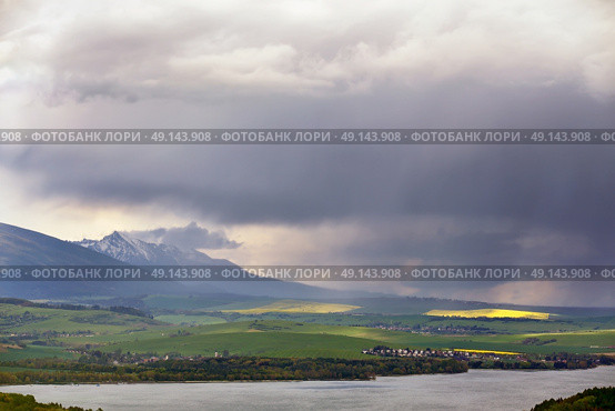 Town on the lake behind the foothills. Spring rain and storm in mountains. Green spring hills of Slovakia. Spring stormy scene. Стоковое фото, агентство Ingram Publishing / Фотобанк Лори