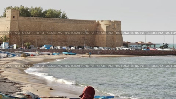 Traditional fishing boats resting on sandy shore Mediterranean Sea in Tunisian town of of Hammamet with sturdy stone historical walls of Kasbah in background. Стоковое видео, видеограф Яков Филимонов / Фотобанк Лори
