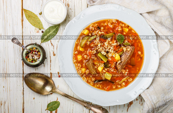Traditional Russian soup Rassolnik beef with pickled cucumbers, potatoes, carrots, onions, tomatoes, pearl barley in bowl on wooden table. Top view. Copy space. Selective focus. Стоковое фото, фотограф Виктория Панченко / Фотобанк Лори