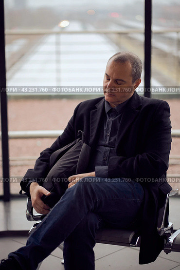 Train Station. Mature man in business clothes is sleeping, sitting in waiting room and waiting for train. Evening is dark. Стоковое фото, фотограф Natalia Gdovskaia / Фотобанк Лори