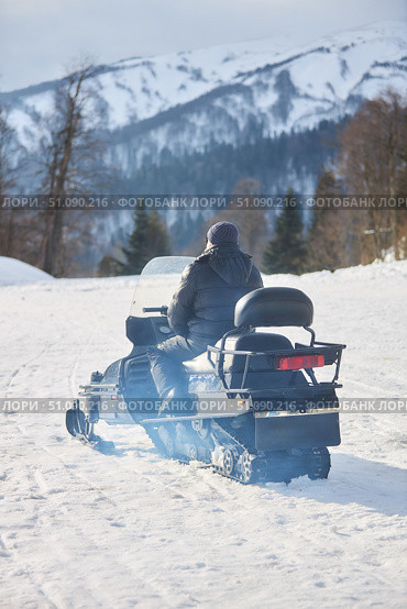 Transport snowmobile with driver on the background of white snow and high mountains. Winter travel in mountainous and forested areas. Стоковое фото, фотограф Наталия Кирсанова / Фотобанк Лори