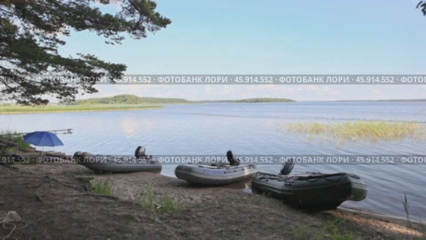 Три надувные лодки с мотором на берегу озера Селигер под голубым небом в солнечный летний день. Редакционное видео, видеограф Сергей Никифоров-Гордеев / Фотобанк Лори