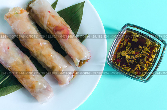 Три свежих спринг-ролла с начинкой из морепродуктов и овощей и темный соус на светло-синем фоне. Стоковое фото, фотограф Лозовая Людмила / Фотобанк Лори