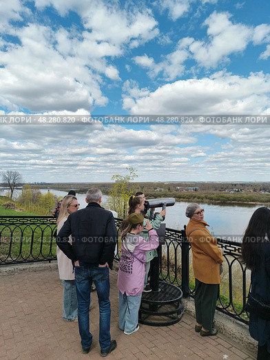 Туристы и подростки в теплой одежде любуются в уличную подзоиную трубу рекой Вяткой в Александровском саду на набережной Грина весной. Редакционное фото, фотограф Светлана Русских / Фотобанк Лори