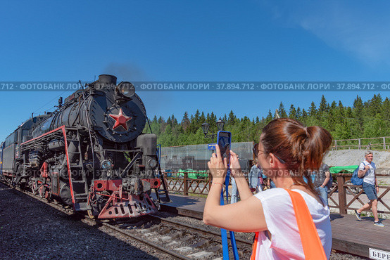Туристы на железнодорожной станции «Горный парк Рускеала» фотографируют ретропоезд на паровозной тяге «Рускеальский экспресс» (2022 год). Редакционное фото, фотограф Румянцева Наталия / Фотобанк Лори