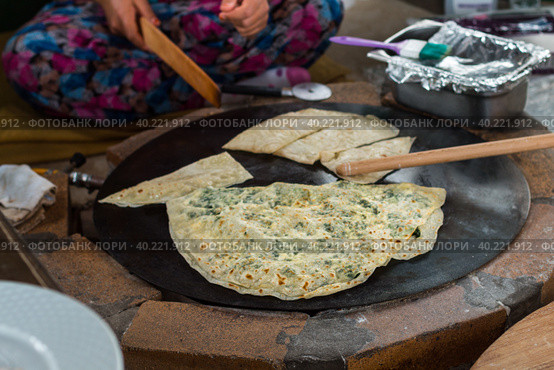 Turkish woman prepares Gozleme - traditional dish in the form of flatbread stuffed with greens and cheese, wrapped inside. Baked in a pan called a saj. Selective focus (2019 год). Стоковое фото, фотограф Виктория Панченко / Фотобанк Лори