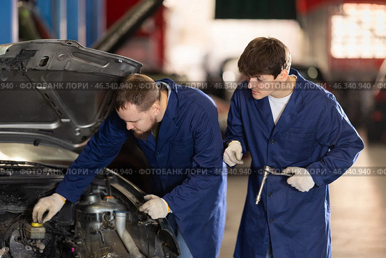 Two auto mechanics work together to diagnose an engine under the hood of a car in repair shop. Стоковое фото, фотограф Яков Филимонов / Фотобанк Лори