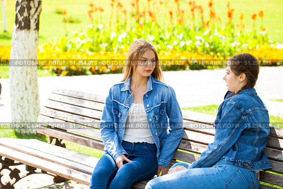 Two beautiful girlfriends are talking in a park sitting on a bench. Стоковое фото, фотограф Андрей Аркуша / Фотобанк Лори