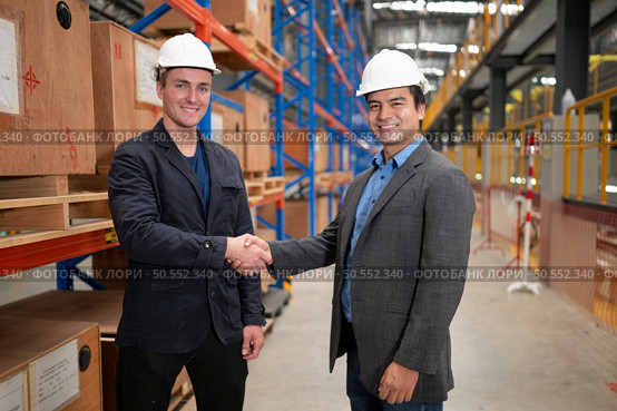 Two businessmen shaking hands in a warehouse It is a warehouse of spare parts and equipment for repairing machinery and passenger cars in the skytrain transportation system. Стоковое фото, агентство Ingram Publishing / Фотобанк Лори