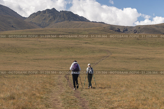 Two climbers go to the mountains through a green meadow. Стоковое фото, фотограф Михаил Яковлев / Фотобанк Лори