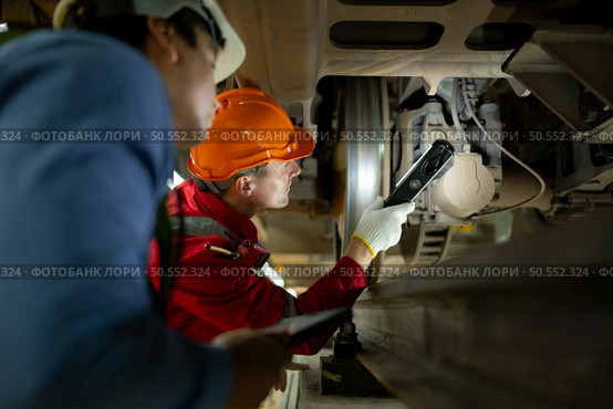 Two engineers for electric trains After detecting difficulties with the electric train’s machinery use searchlights to locate and check damaged sections. In the electric train repair shop. Стоковое фото, агентство Ingram Publishing / Фотобанк Лори