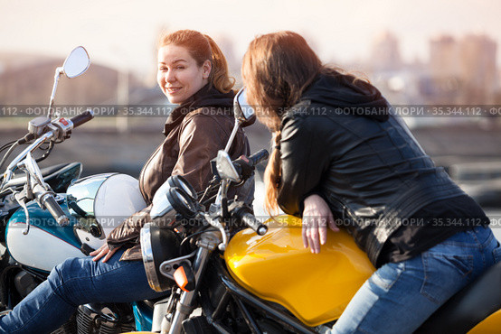 Two European women motorcyclists talking cheerfully while sitting on their motorcycles. Стоковое фото, фотограф Кекяляйнен Андрей / Фотобанк Лори