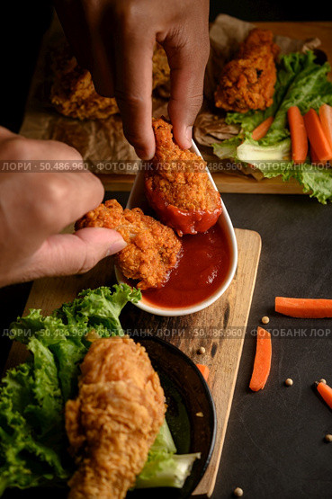 Two hand holding crispy fried chicken dipped in tomato sauce.Selective focus. Стоковое фото, агентство Ingram Publishing / Фотобанк Лори