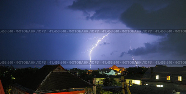 Two lightning bolts against the background of a dark sky with clouds. Thunderstorm over the city. Discharges of thunder and lightning over the rooftops. Thunderstorm front, typhoon or cyclone. Стоковое фото, фотограф Юлия Петровская / Фотобанк Лори