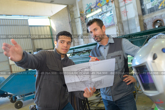 two male engineers in discussion while holding scale drawings. Стоковое фото, агентство Ingram Publishing / Фотобанк Лори