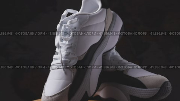 Two white women's sneakers on a wooden surface. Dark background. The camera flies around. Parallax effect. Close-up. Krasnodar, Russia, April 19, 2022. Редакционное видео, видеограф Воловодов Владимир / Фотобанк Лори