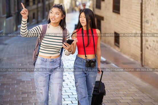 Two young Chinese women passing by guided by the GPS of their smartphone, through the streets of Granada, Spain. Concept of Asian people traveling in Europe.. Asian female travelers pointing away while walking on street. Стоковое фото, агентство Ingram Publishing / Фотобанк Лори