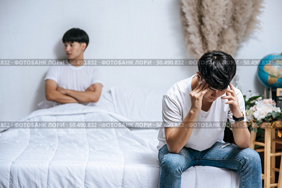 Two young men were angry on the bed and the other sat at the edge of the bed and was stressed. Стоковое фото, агентство Ingram Publishing / Фотобанк Лори