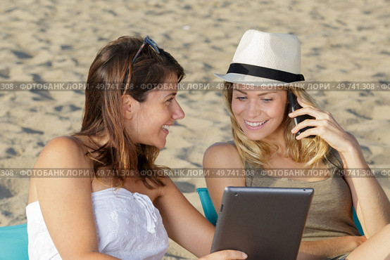 two young woman on beach with tablet and smartphone. Стоковое фото, агентство Ingram Publishing / Фотобанк Лори