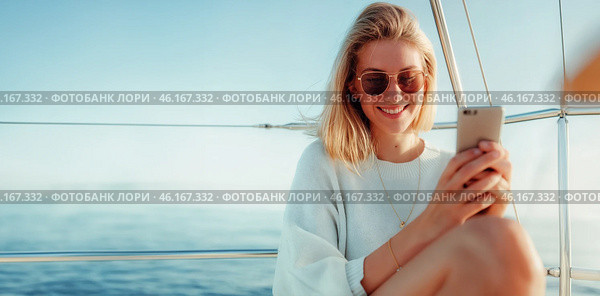 Улыбающаяся женщина делает селфи и ведёт соцсети на яхте, наслаждаясь морским путешествием. Стоковое AI-изображение, AI-художник Anna Leeva / Фотобанк Лори