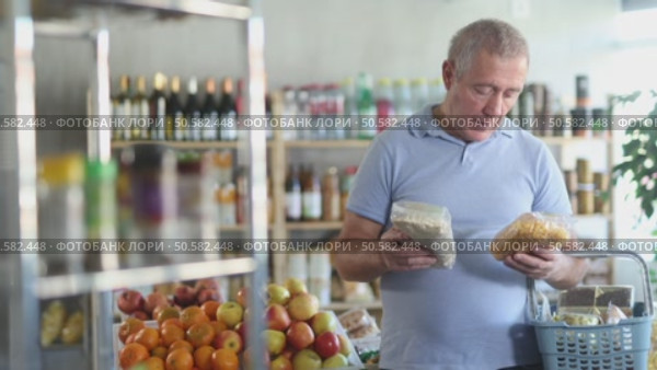 Uncertain mature male buyer choosing a package of flakes in grocery shop. Стоковое видео, видеограф Яков Филимонов / Фотобанк Лори