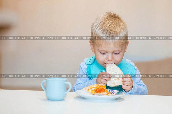 Unhealthy food for children. Eating. A cute 2-year-old kid eats pizza for lunch. Fast food. Family and children. Стоковое фото, фотограф Photojuli / Фотобанк Лори