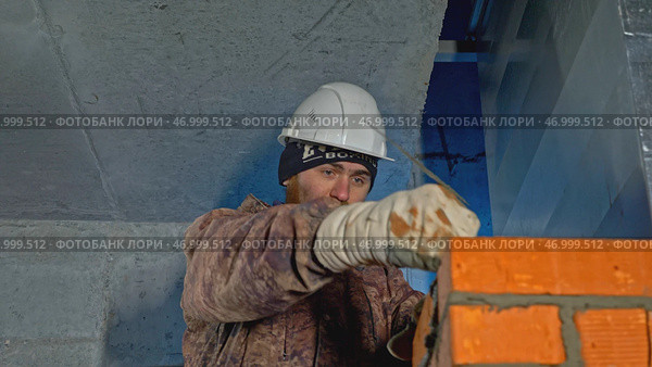 Uniformed worker makes brickwork inside house. Стоковое фото, фотограф David Kashakhi / Фотобанк Лори