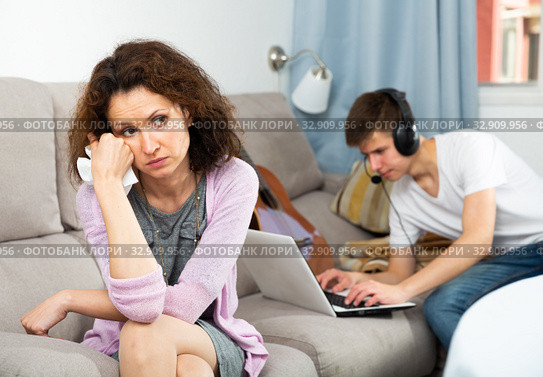 Upset woman on background with son playing on laptop. Стоковое фото, фотограф Яков Филимонов / Фотобанк Лори