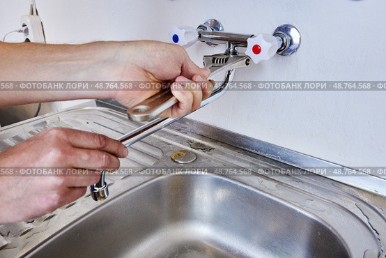 Using adjustable wrench plumber tightens mounting nut of spout on dual handle wall mounted faucet with hidden pipework inside wall. Стоковое фото, фотограф Владимир Григорьев / Фотобанк Лори