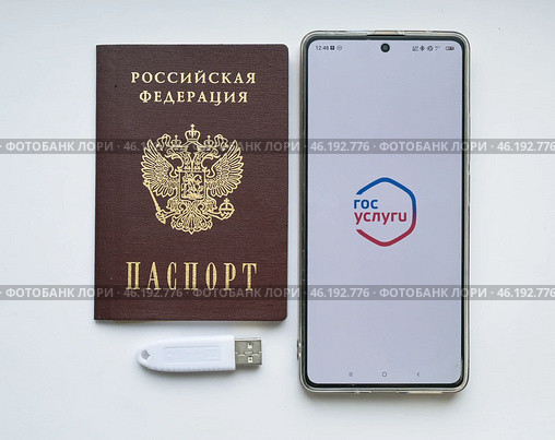 Устройство  USB eToken  (рутокен) белого цвета, устройство для хранения электронной цифровой подписи (ЭЦП) и информации для аутентификации пользователя, паспорт и телефон с приложением Госуслуги на белом фоне. Редакционное фото, фотограф Snezka / Фотобанк Лори
