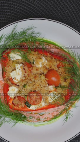 Vegetarian gourmet bell pepper filled with couscous, feta, zucchini, tomatoes, spinning slowly on white ceramic plate, dark backdrop. Стоковое видео, видеограф Данил Руденко / Фотобанк Лори