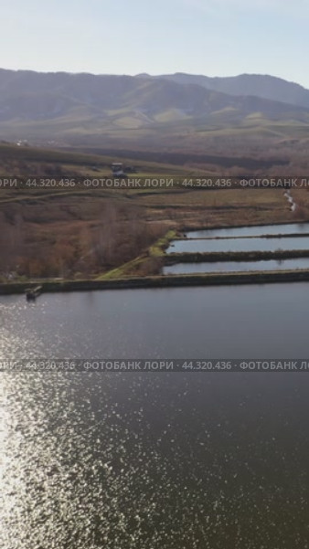 Vertical drone video of flying over a hilly rural landscape with a winding road and fish ponds. Altai Krai. Стоковое видео, видеограф Сергей Пристяжнюк (Serg Zastavkin) / Фотобанк Лори