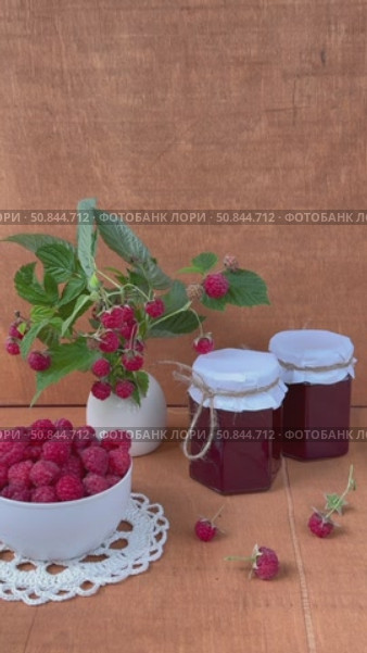 Vertical video of ripe freshly picked raspberries in bowl, jars of homemade jam and bouquet of raspberry branches with berries on wooden garden tableon on summer day. Harvesting organic  berries. Стоковое видео, видеограф Виктория Катьянова / Фотобанк Лори