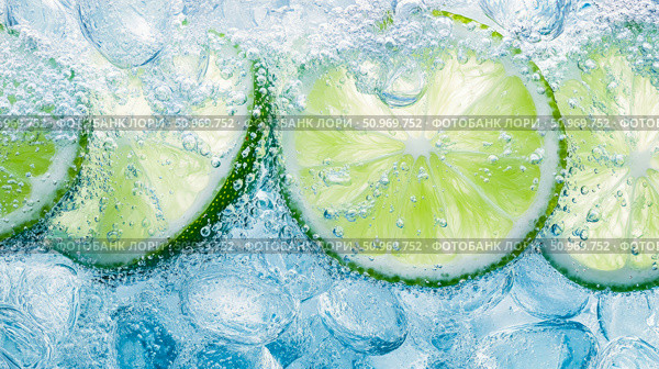 Vibrant green lime citrus slices and clear ice cubes immersed in effervescent, crystal-clear carbonated water with abundant bubbles, creating a cool and refreshing beverage background. Стоковое AI-изображение, AI-художник Данила Большаков / Фотобанк Лори