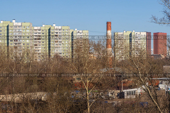 Вид на многоэтажные панельные жилые дома. На переднем плане деревья и промышленная труба. Жилые кварталы в спальном районе большого города. Городские окраины. Стоковое фото, фотограф Андрей Степанов / Фотобанк Лори