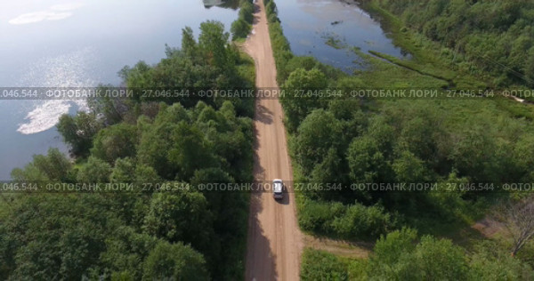 Вид сверху на автомобиль, проезжающий по грунтовой дороге среди леса и водоема. Стоковое видео, видеограф Кекяляйнен Андрей / Фотобанк Лори