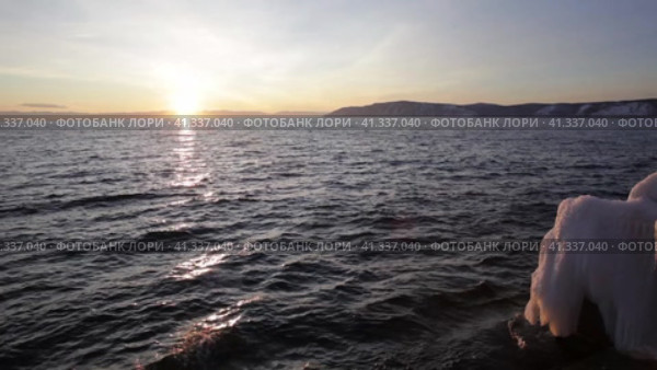 Video of Baikal Lake at sunset in December. Waves crash against an icy pier against the backdrop of the setting sun. Beautiful seascape. Natural background. Travels along the lake shore. Стоковое видео, видеограф Виктория Катьянова / Фотобанк Лори