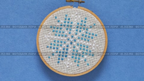 Video of hand embroidered cross stitch snowflake in wooden hoop on blue background. Winter crafts, needlework and Christmas gifts concept. Cross stitches as a hobby. Flat lay, close-up. Стоковое видео, видеограф Виктория Катьянова / Фотобанк Лори