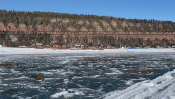 Video of Siberian river Irkut in November during freeze-up. Ice floes float on blue water. On shore is Shamanka village near famous Shamansky cliff, called 33 heroes bogatyrs - natural landmark. Стоковое видео, видеограф Виктория Катьянова / Фотобанк Лори